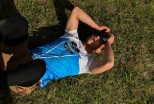 A man lies on green grass outdoors with covered eyes, conveying relaxation.