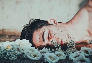 A contemplative image of a man lying among white flowers, conveying introspection.
