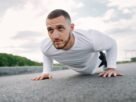 Focused man in sportswear doing push-ups on a road in a natural setting.