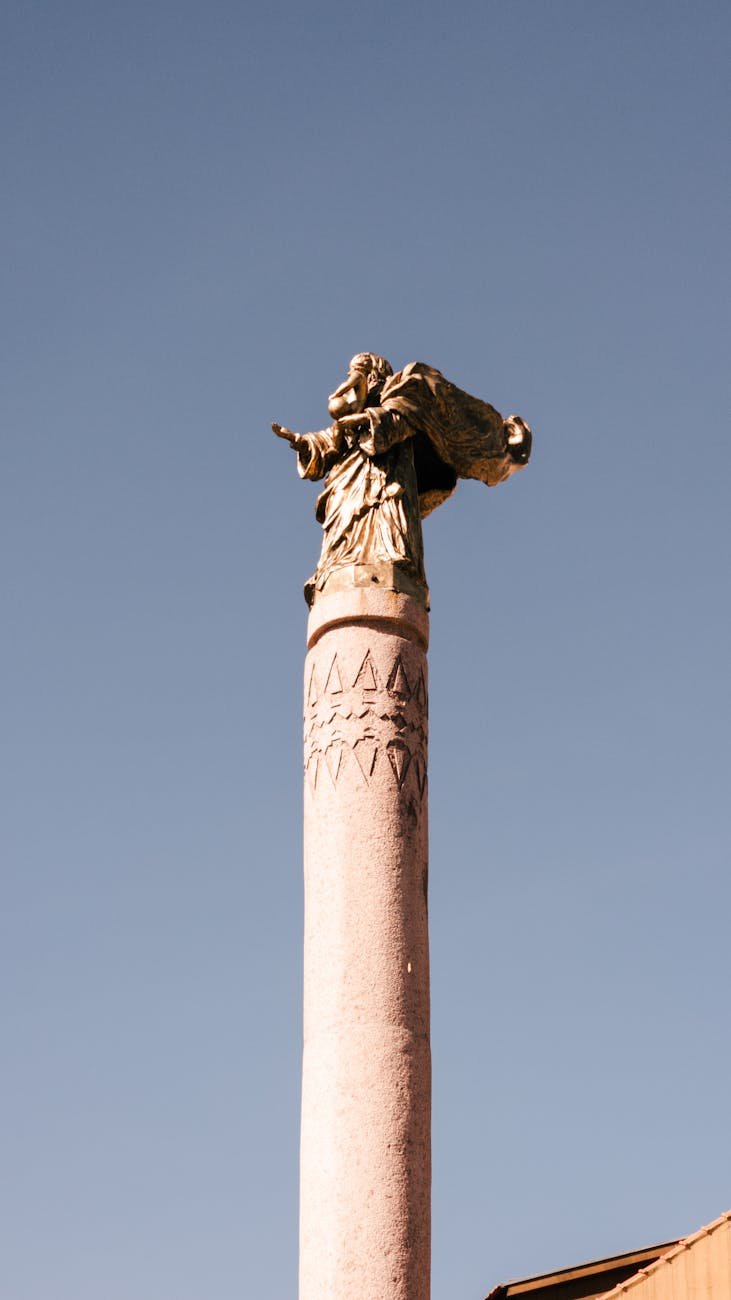 A classic statue atop a column against a clear blue sky in Curitiba, Brazil.